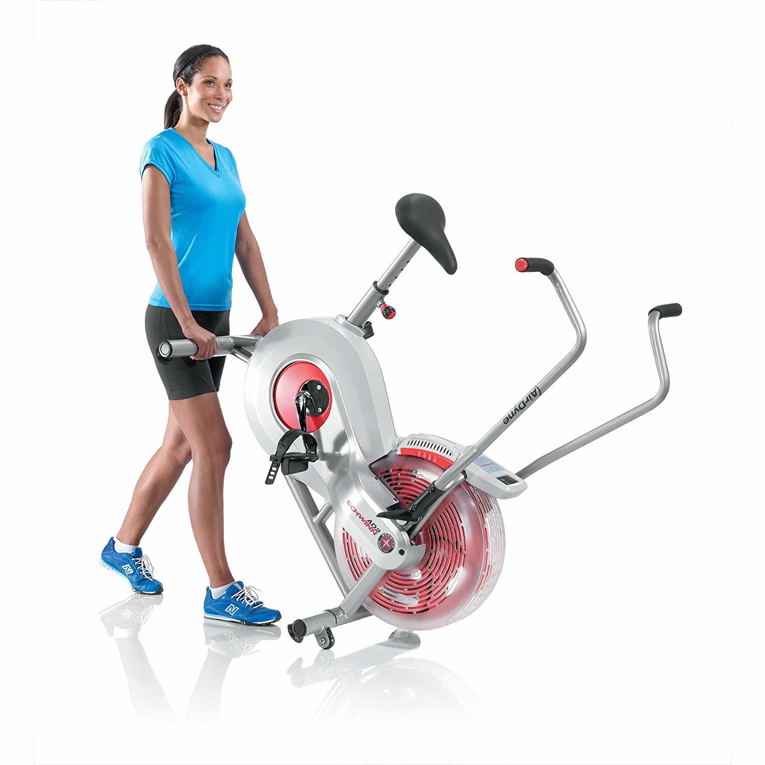 A woman in athletic clothes moving an exercise bike using its roller wheels.